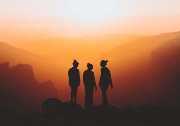 Three people on a mountain at sunrise